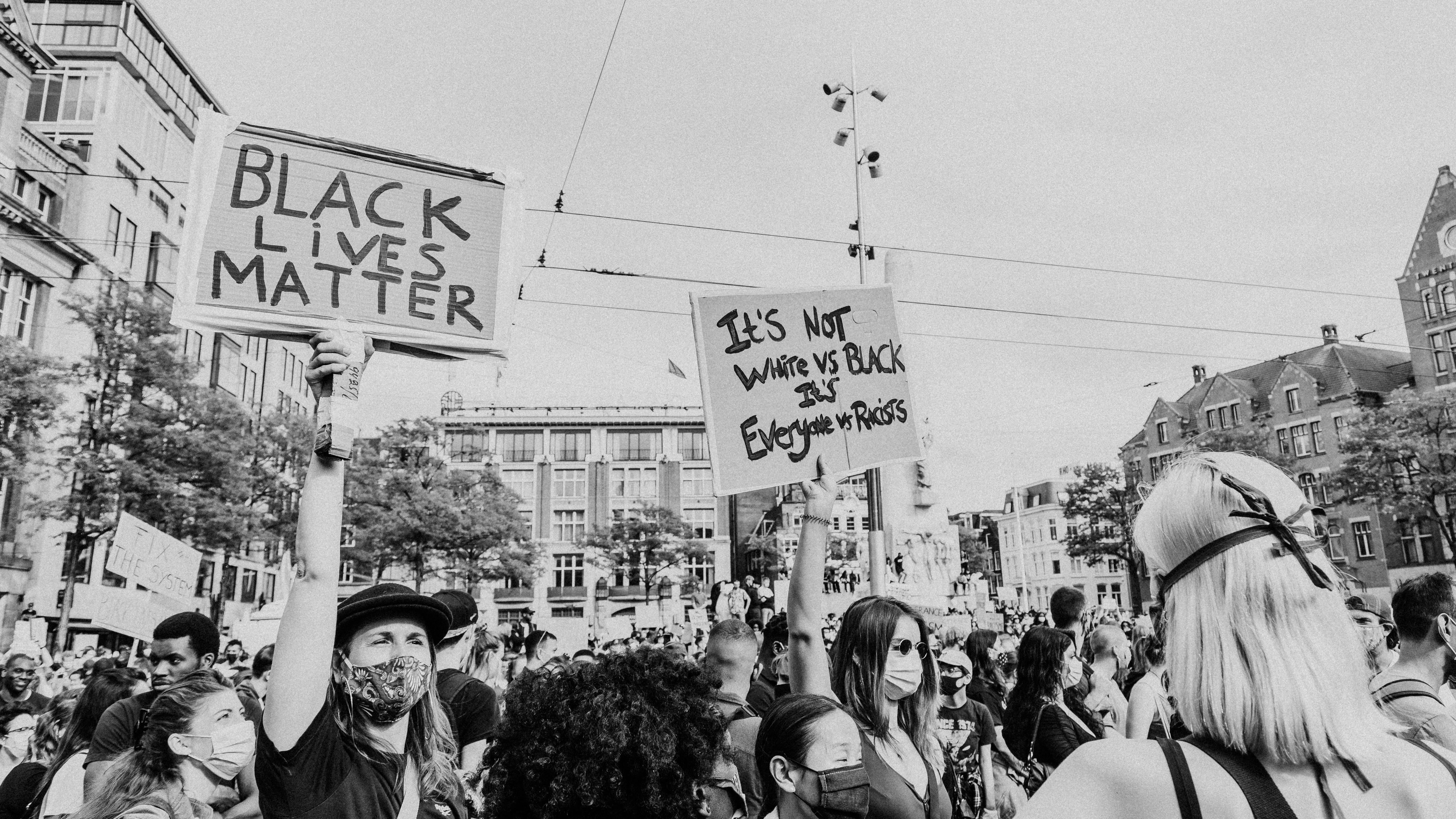 Black Lives Matter protest crowd with signs reading It's Not White vs Black It's Everyone vs Racists